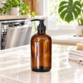 16 oz amber glass bottle of PurposeFill dishwasher gel with black pump top in a light, bright kitchen setting.